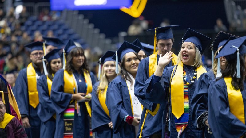 Estudiantes en gorras de graduación y togas parados en una línea para recibir sus diplomas.