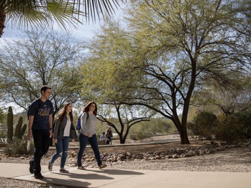 Tres estudiantes caminan juntos afuera en un campus de NAU.