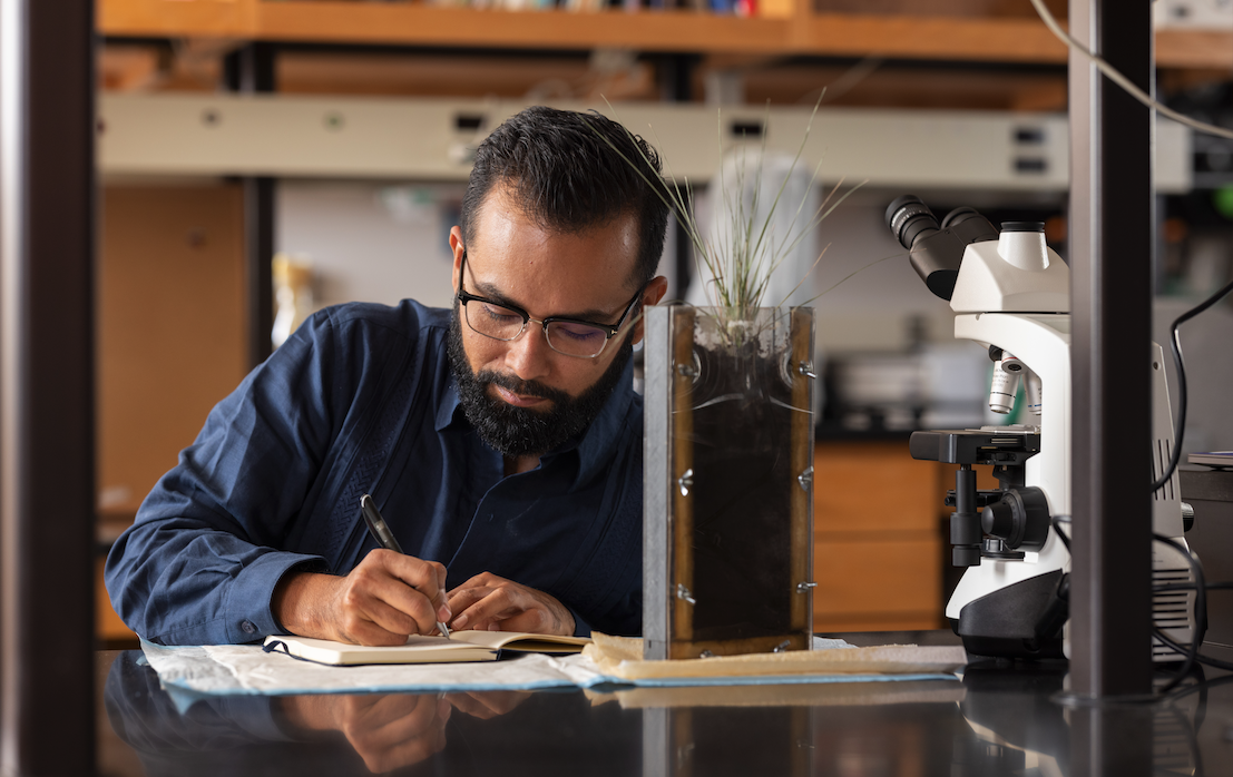 Investigador de ecología forestal Javier Ceja-Navarro escribe en una libreta en su laboratorio cerca de una muestra de suelo y microscopio.