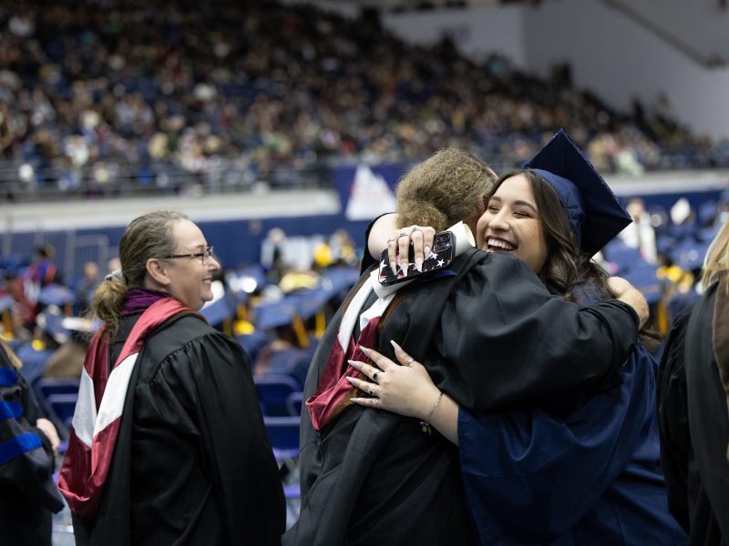 En una ceremonia de graduación de NAU, un nuevo graduado abraza a un miembro de la facultad.