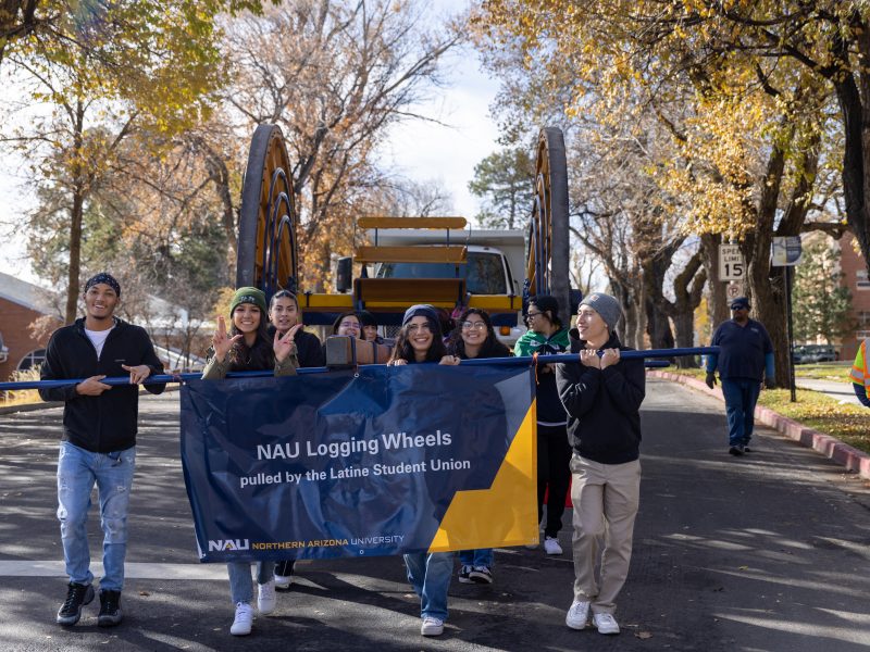 Representantes de NAU Logging Wheels organización estudiantil caminan en el desfile de Homecoming.