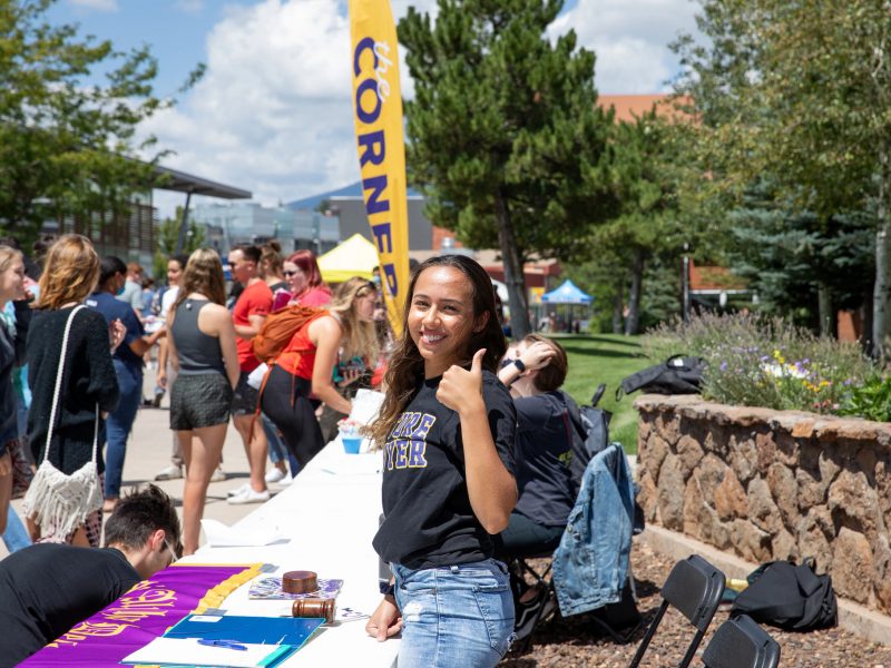 Un estudiante da una señal de aprobación mientras repartiendo información sobre clubes de estudiantes de NAU en el campus.