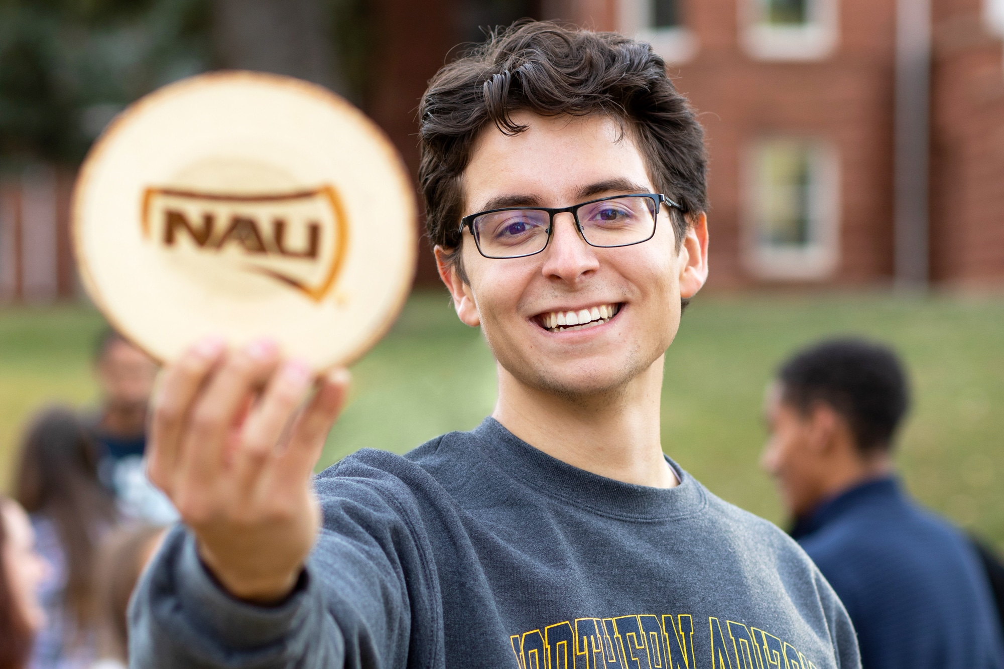NAU student wearing an NAU sweatshirt, holding a round piece of wood with the NAU logo on it