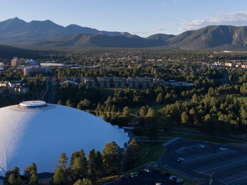 Aerial picture of NAU Skydome and campus taken from the air with the San Francisco Peak mountains in the background
