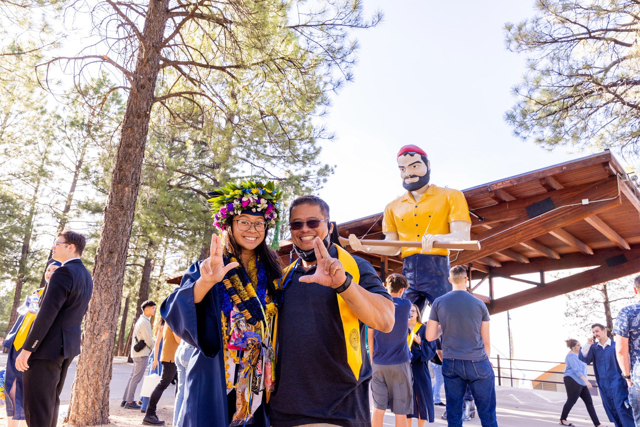 An NAU student and her dad, standing outside the Skydome in front of the Louie statue, giving the LJ sign with their hands