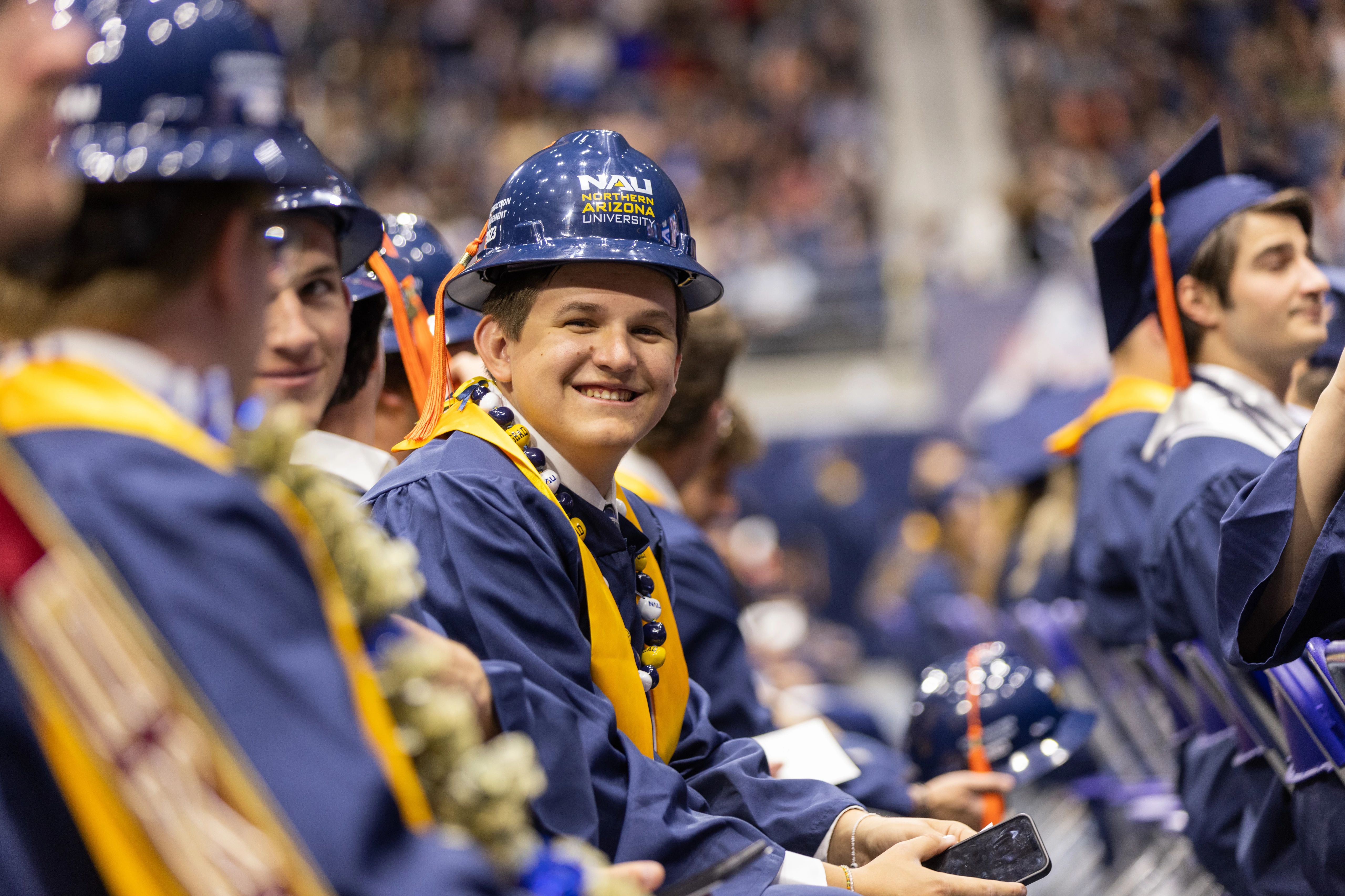 NAU students sitting at commencement wearing construction hardhats with the NAU logo on them