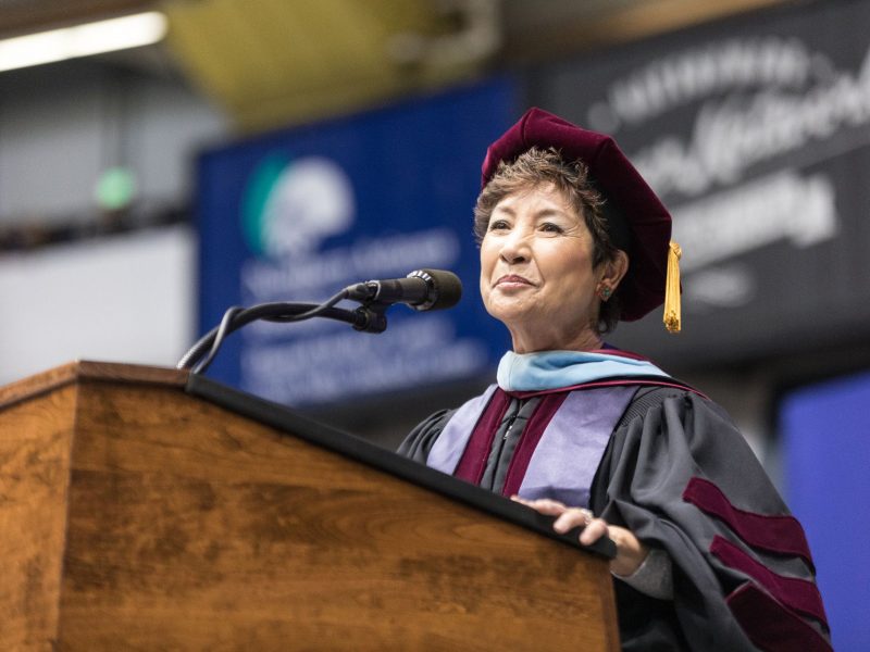 Faculty member wearing regalia delivering speech during NAU commencement