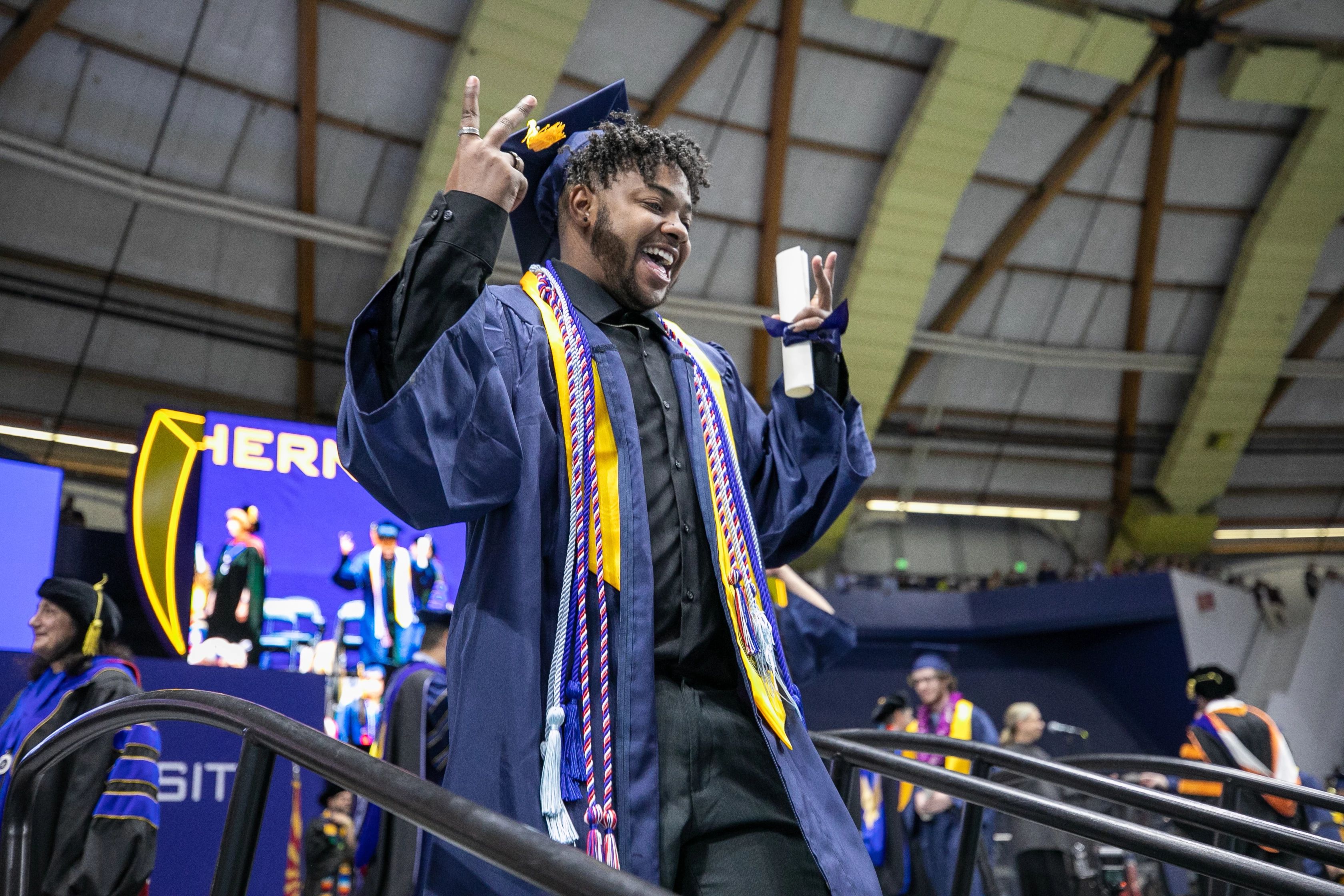 African American NAU student leaving the stage with his diploma in hand, giving a peace sign with his fingers
