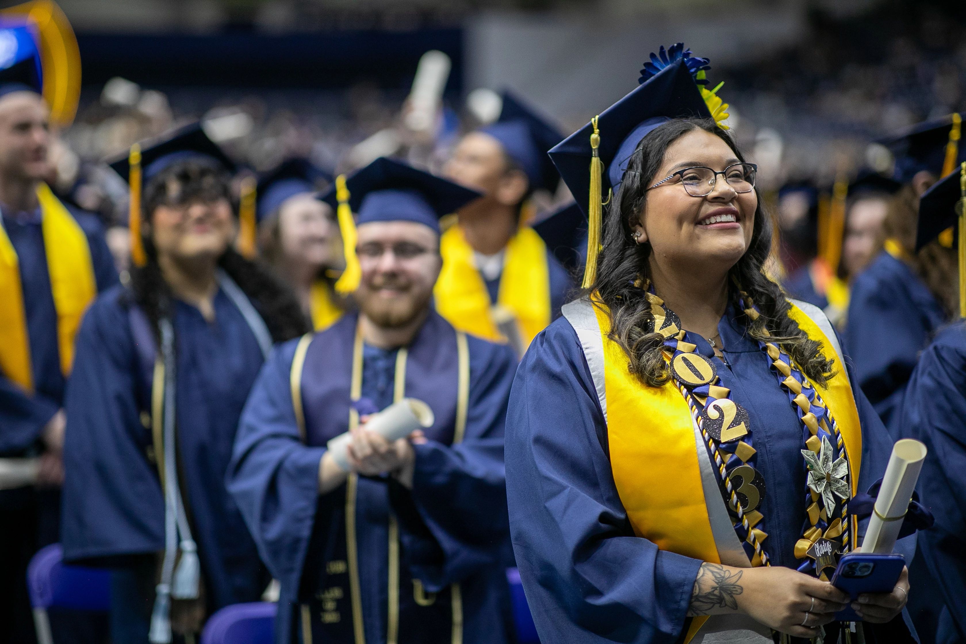 NAU grads standing, smiling, and holding their diplomas at the end of Commencement