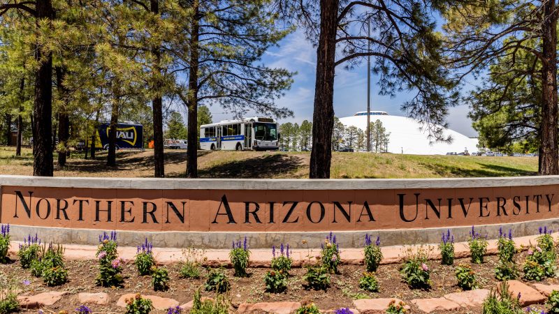 NAU marquee with campus bus and pine trees in the background