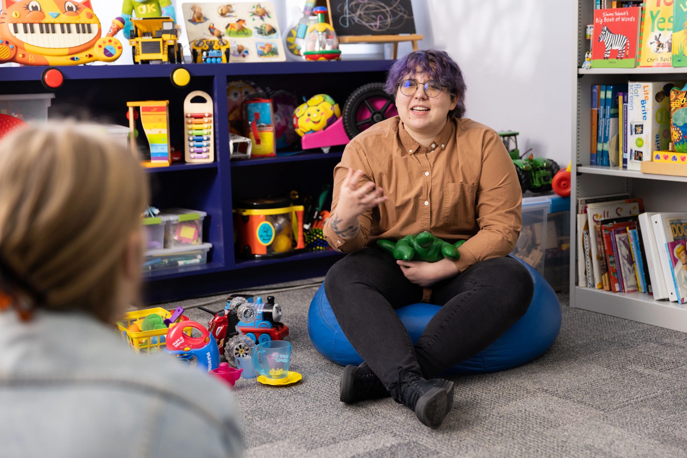 NAU college of education student sitting on a beanbag in a classroom setting, talking to a classmate