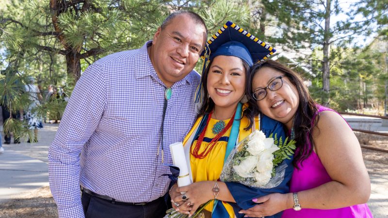 NAU grad in cap and gown standing with mom and dad outside