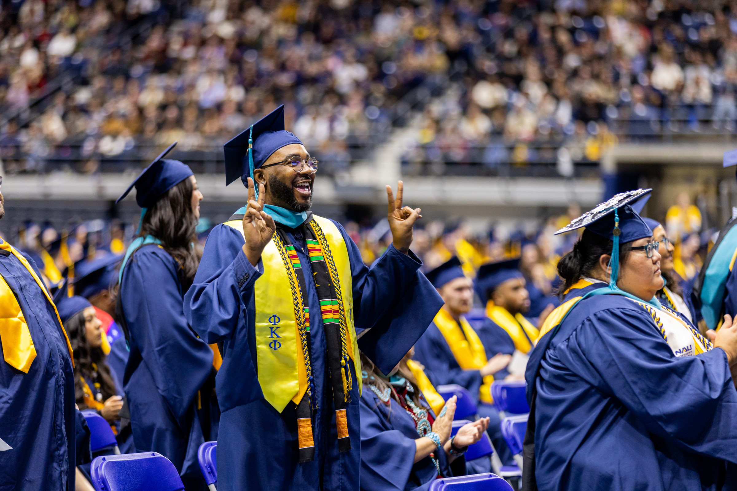 Male graduate standing and raising both hands giving the peace symbol with his fingers