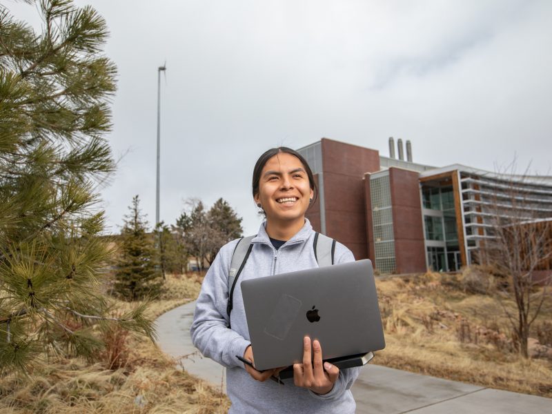 Student smiling happily as he walks away from Northern Arizona University Flagstaff campus with a computer.