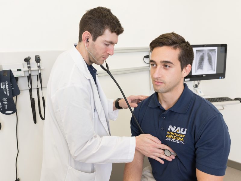 A physician assistant listens to a patients heartbeat through a stethoscope.