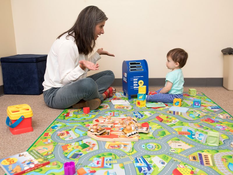 Dr. Anna Sosa and a toddler sit facing each other on a play mat.