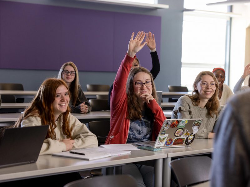 Students participating in class; a few of them raise their hand.