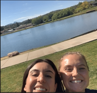 Two students smile outside by a lake