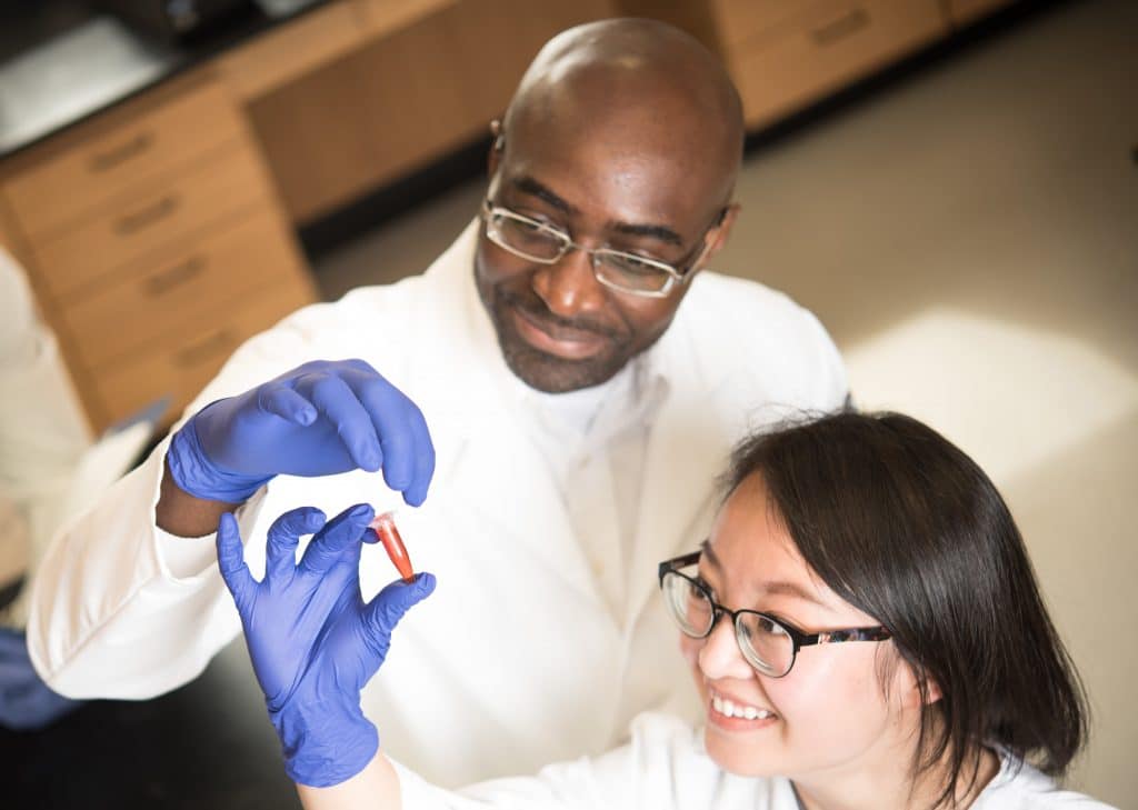 Two scientists in lab coats examining a vile.