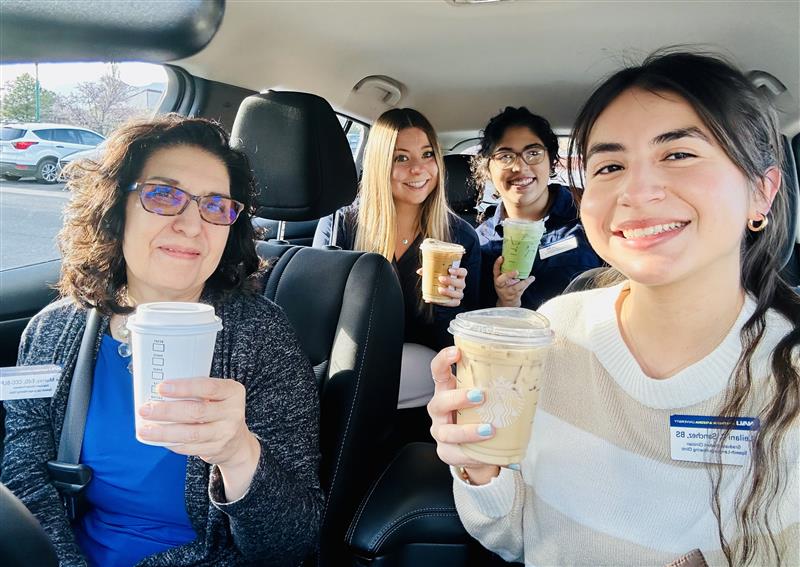 NAU Communication Sciences and Disorders students and professor Fe Murray holding coffee and smiling inside a vehicle.