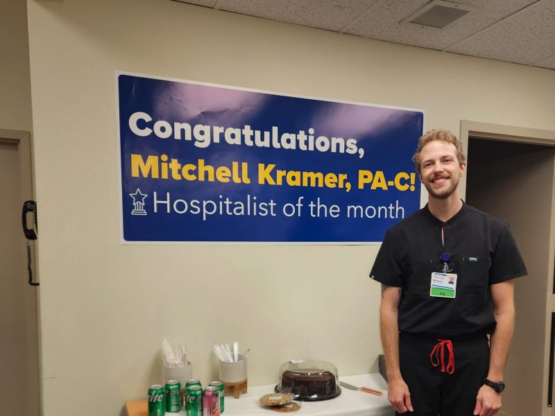 Mitchell Kramer, graduate of the NAU Physician Assistant Studies program, standing next to a congratulations banner for Hospitalist of the Month for MedStar Health.