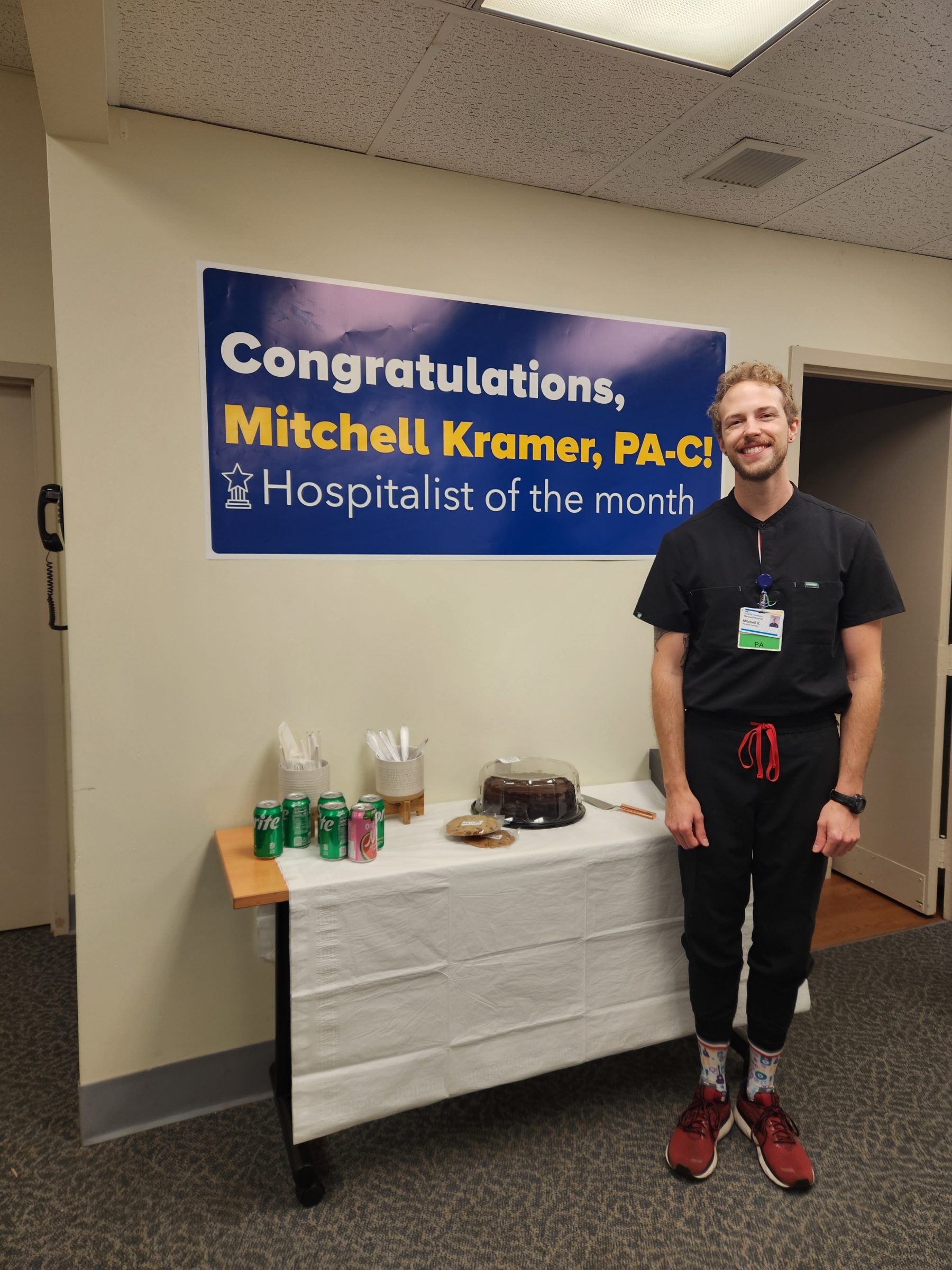 Mitchell Kramer, graduate of the NAU Physician Assistant Studies program, standing next to a congratulations banner for Hospitalist of the Month for MedStar Health.