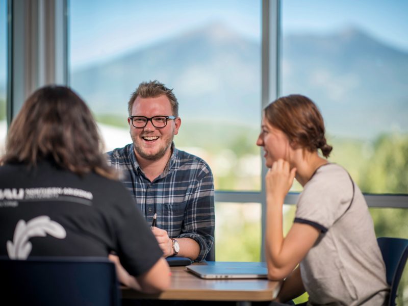 N A U students laughing in a group setting indoors with a window background.