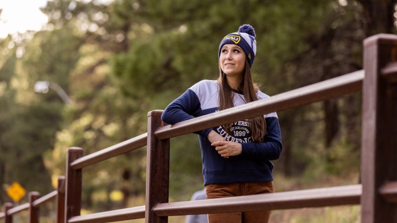 Student smiling and looking over to the distance while outdoors on a trail, wearing N A U gear.