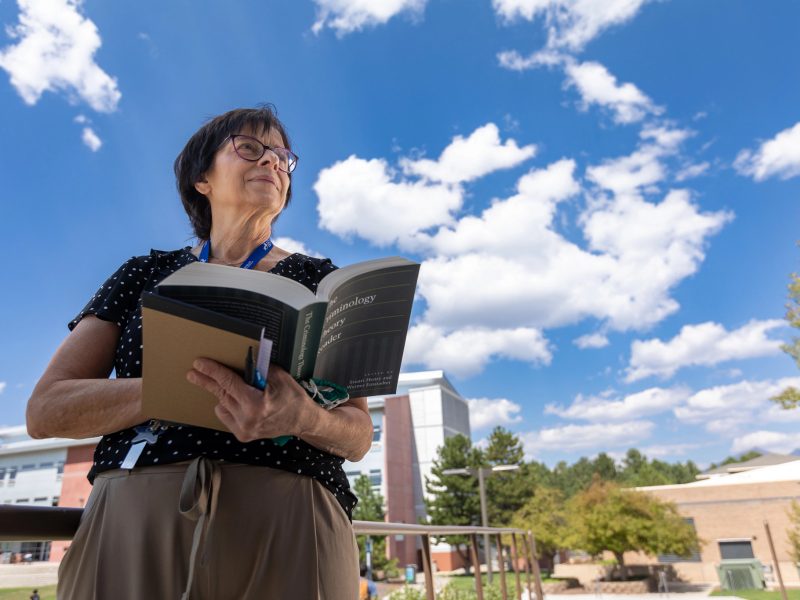 Faculty reading a book outdoors.