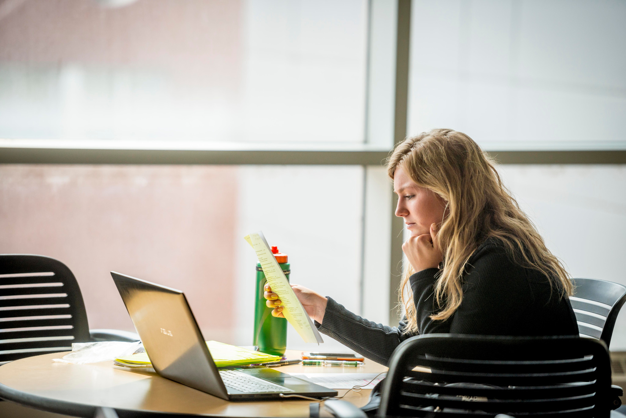 Student working on a laptop with a large window in the background.