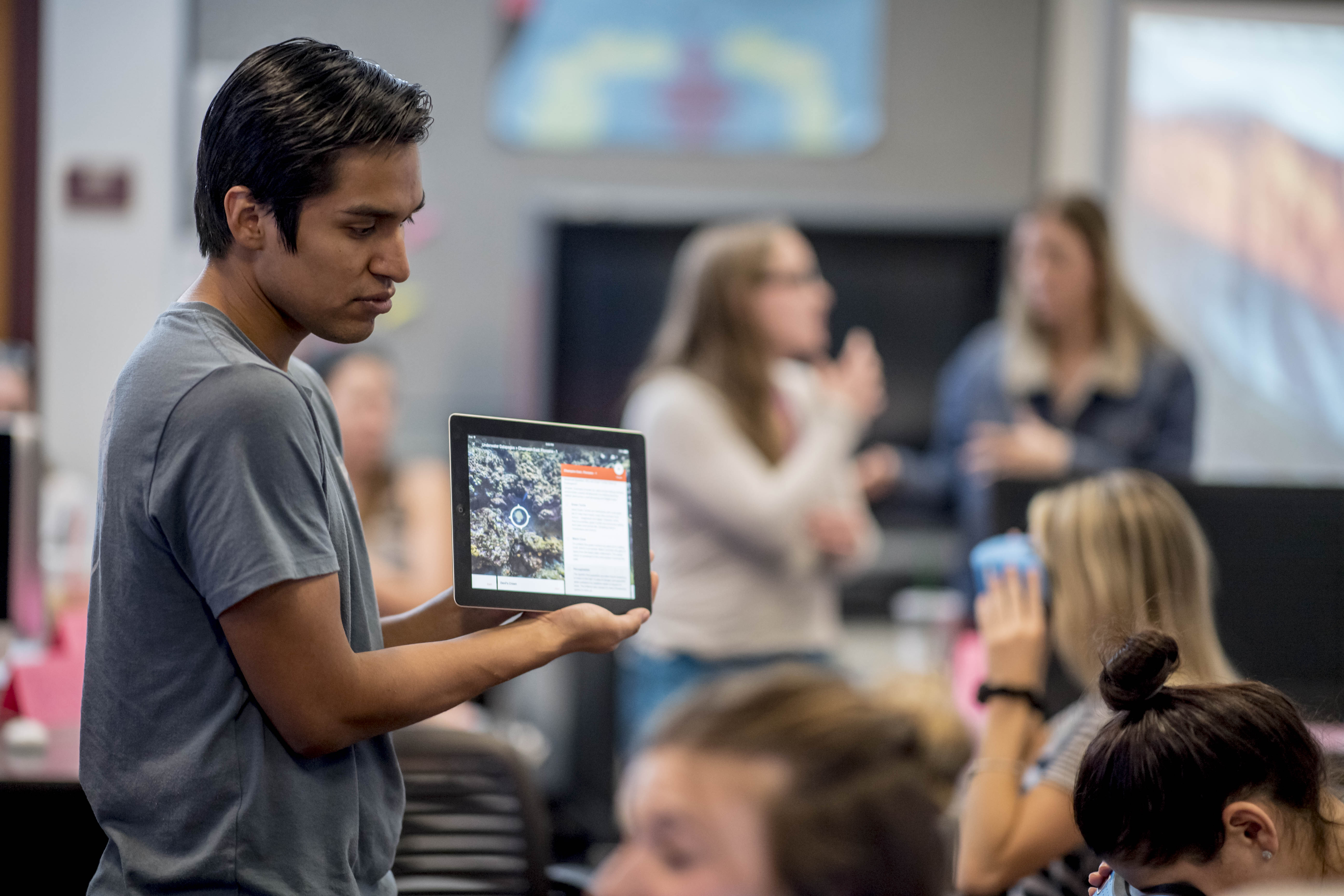 N A U student is standing in front of other student holding a tablet.