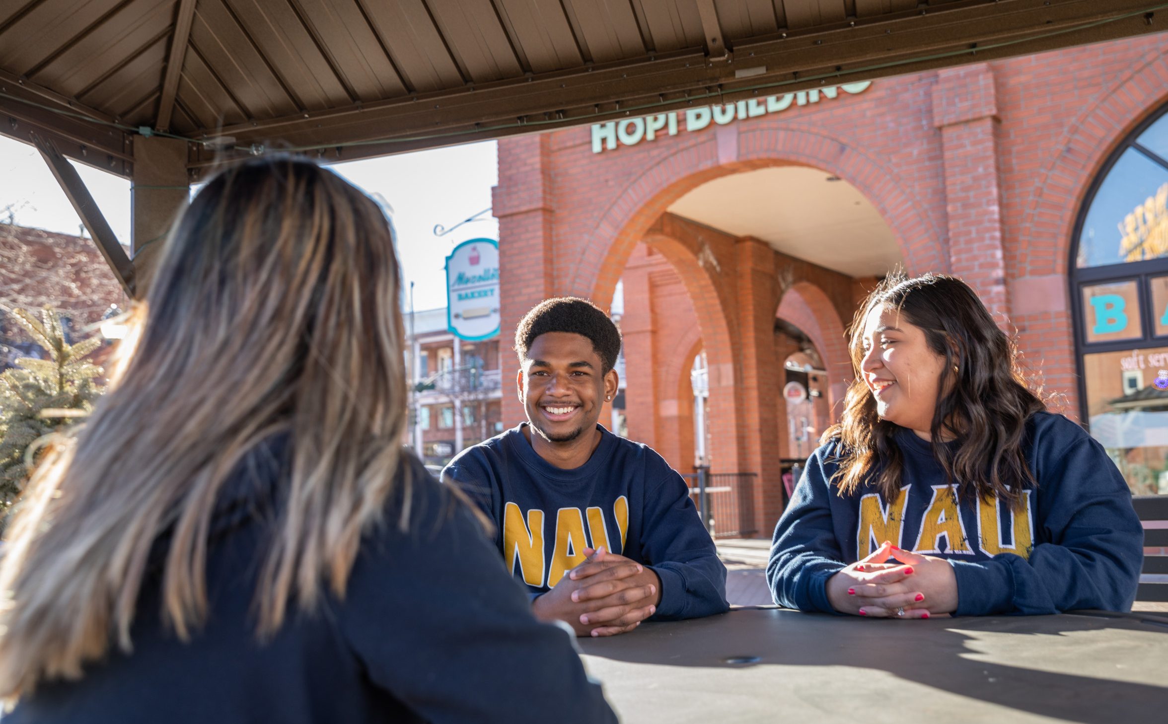 Three students sitting at a table outside talking to each other.