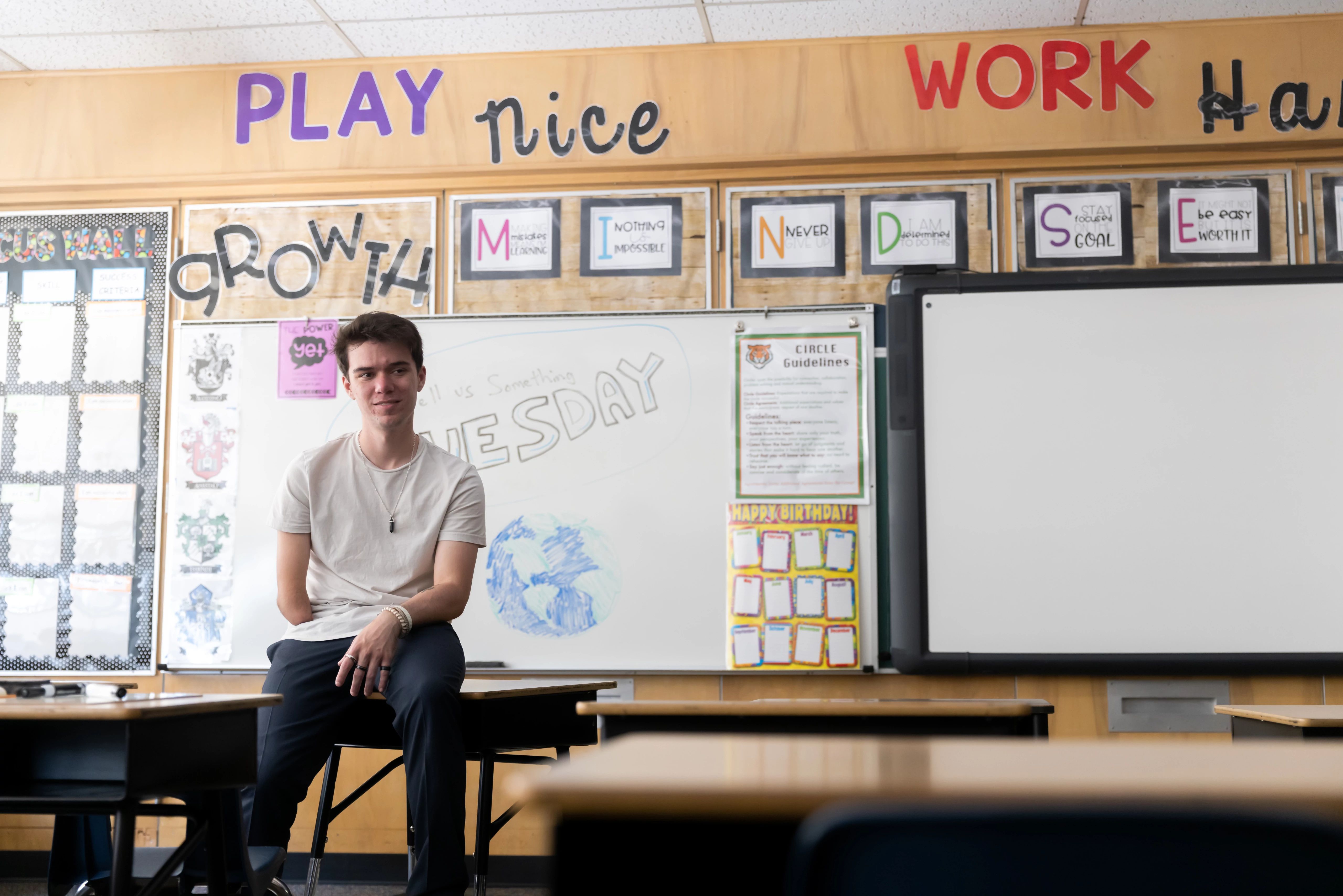Student teacher sitting on a desk in front of classroom.