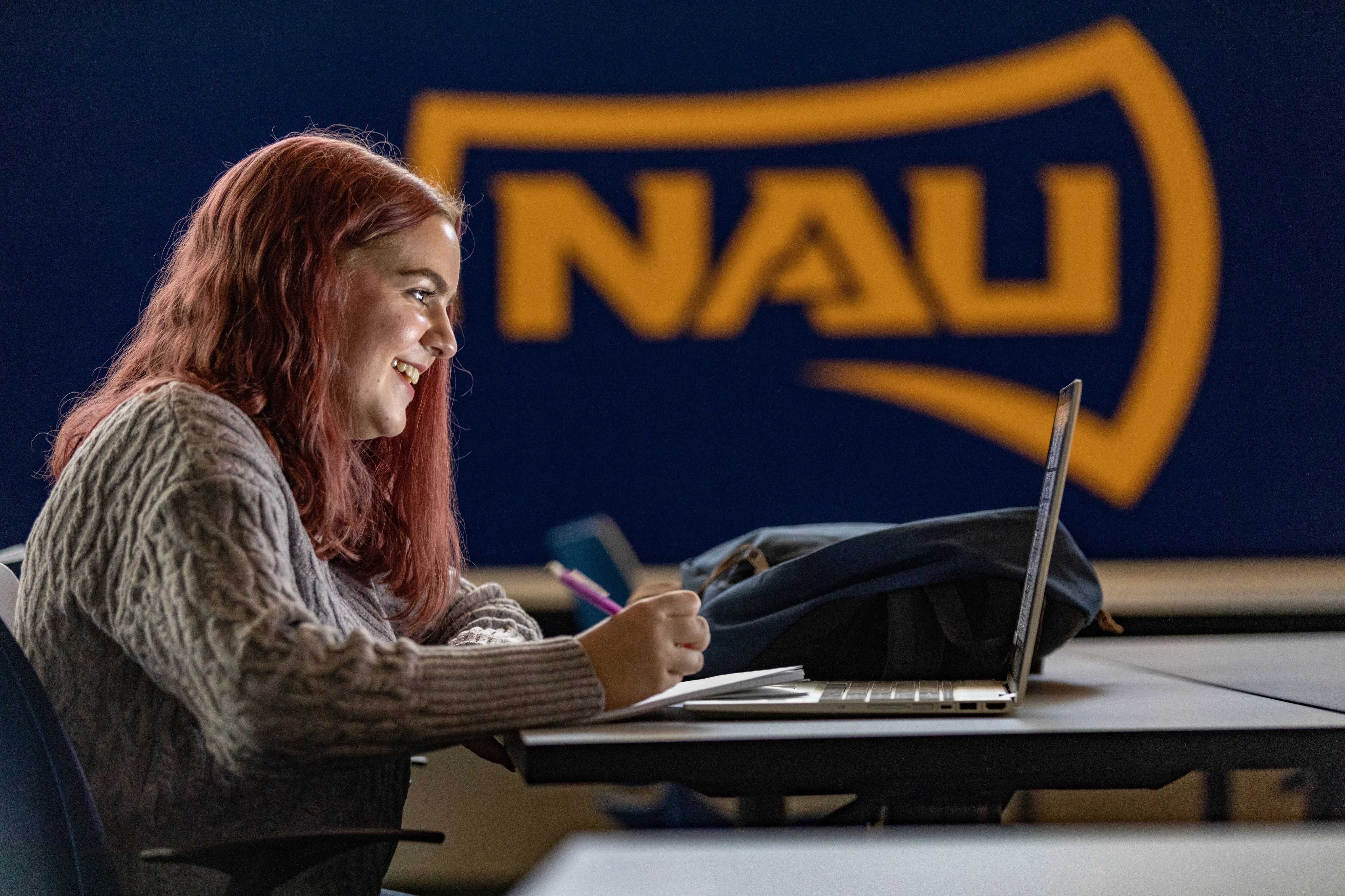N A U student smiles while working on their laptop.