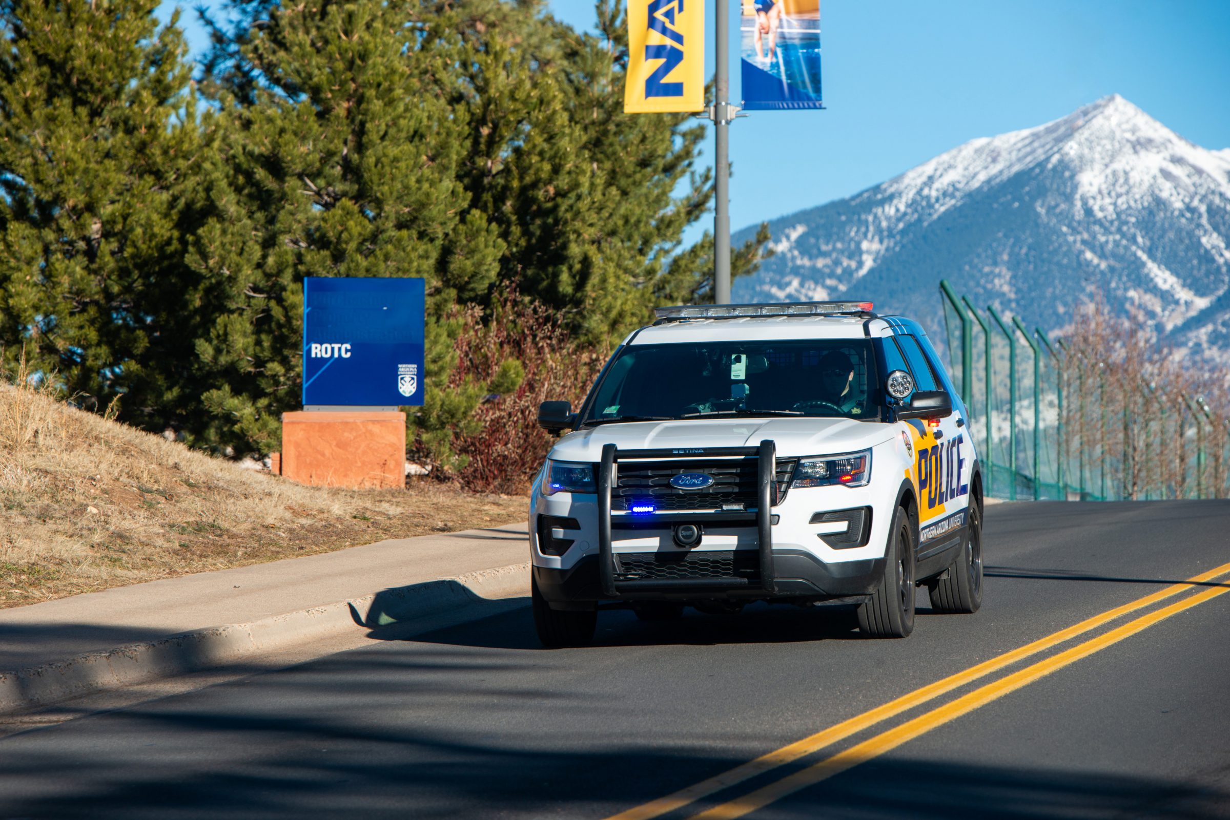 A police vehicle drives through campus with a snow capped mountain in the background.