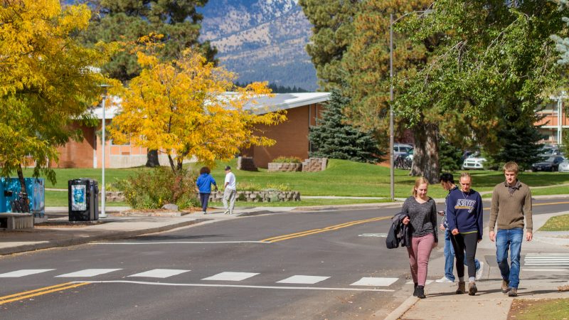 Students walk on a sidewalk at N A U campus during Fall season.