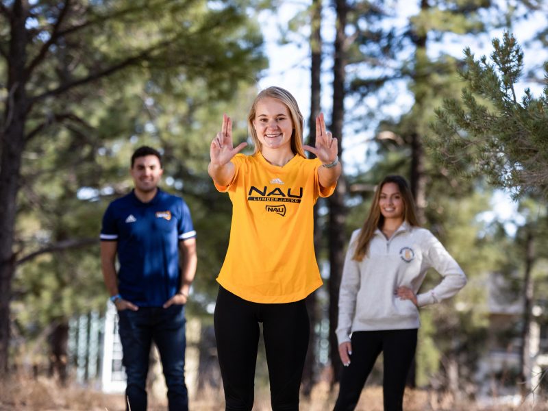 A photo of students wearing NAU shirts posing with the "Lumberjacks" sign.