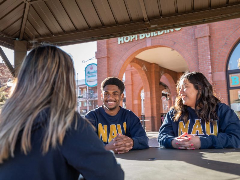 Three students conversing outside at a table.