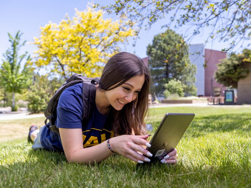 Smiling student Molly Garguilo reads tablet and lays on grassy lawn.