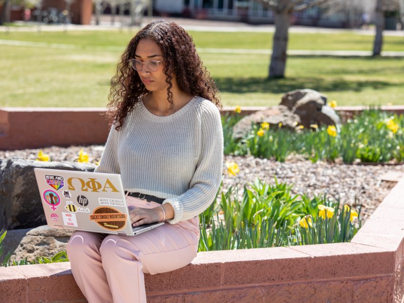 A photo of a student working on her laptop outside on a sunny day at Flagstaff campus.