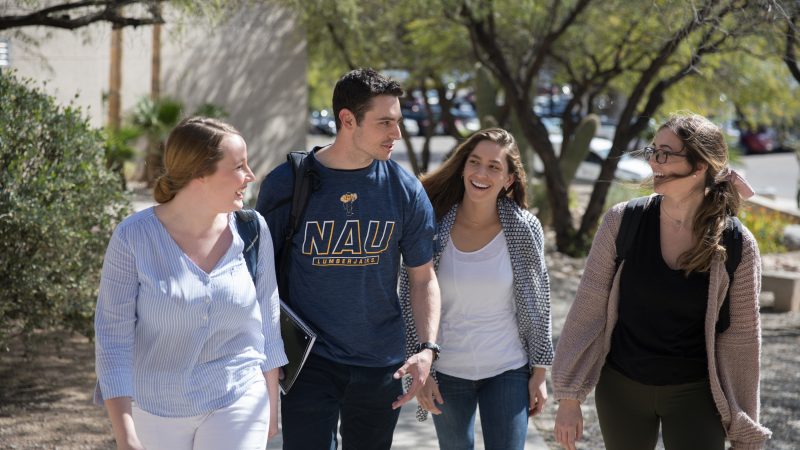 A group of four students walk on a sidewalk at Pima Community College.