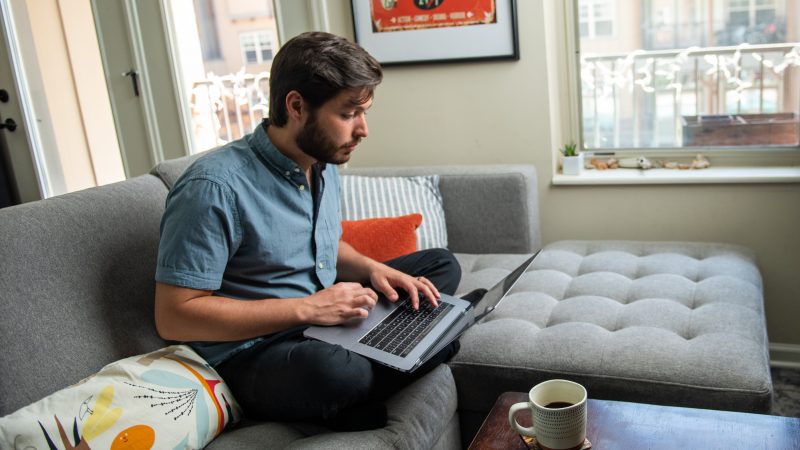 Student studies on laptop while sitting on couch.