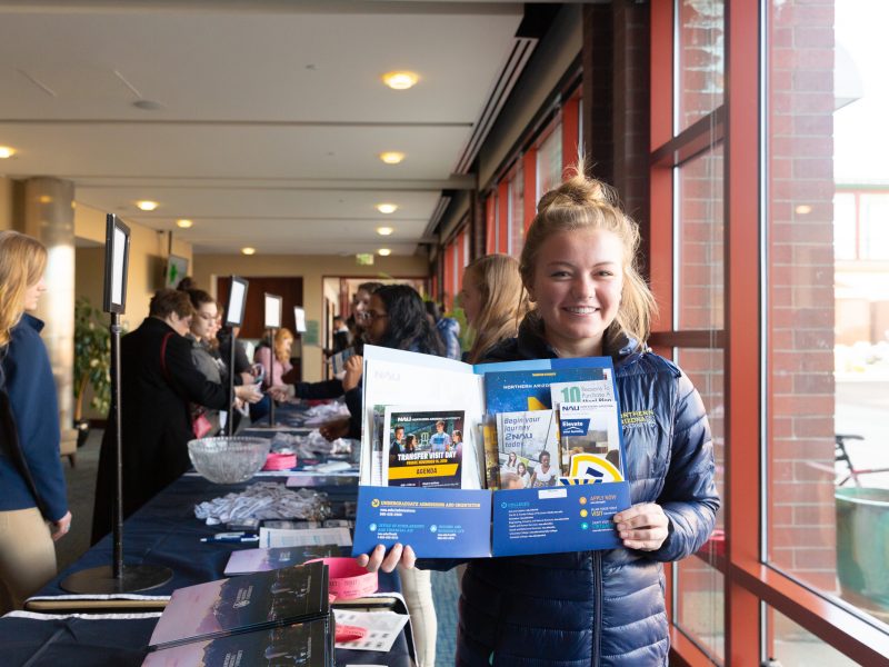 A photo of a student smiling while holding an NAU Orientation packet.