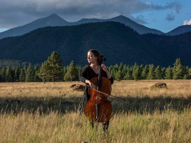 A student plays the cello surrounded by pine trees in Flagstaff