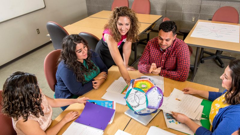 Five people smile as the work together reviewing assignments