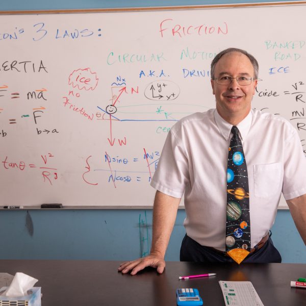 Faculty smiling to the camera with math on the white board behind him.
