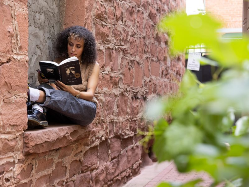 Student reading a book on the side of the wall.