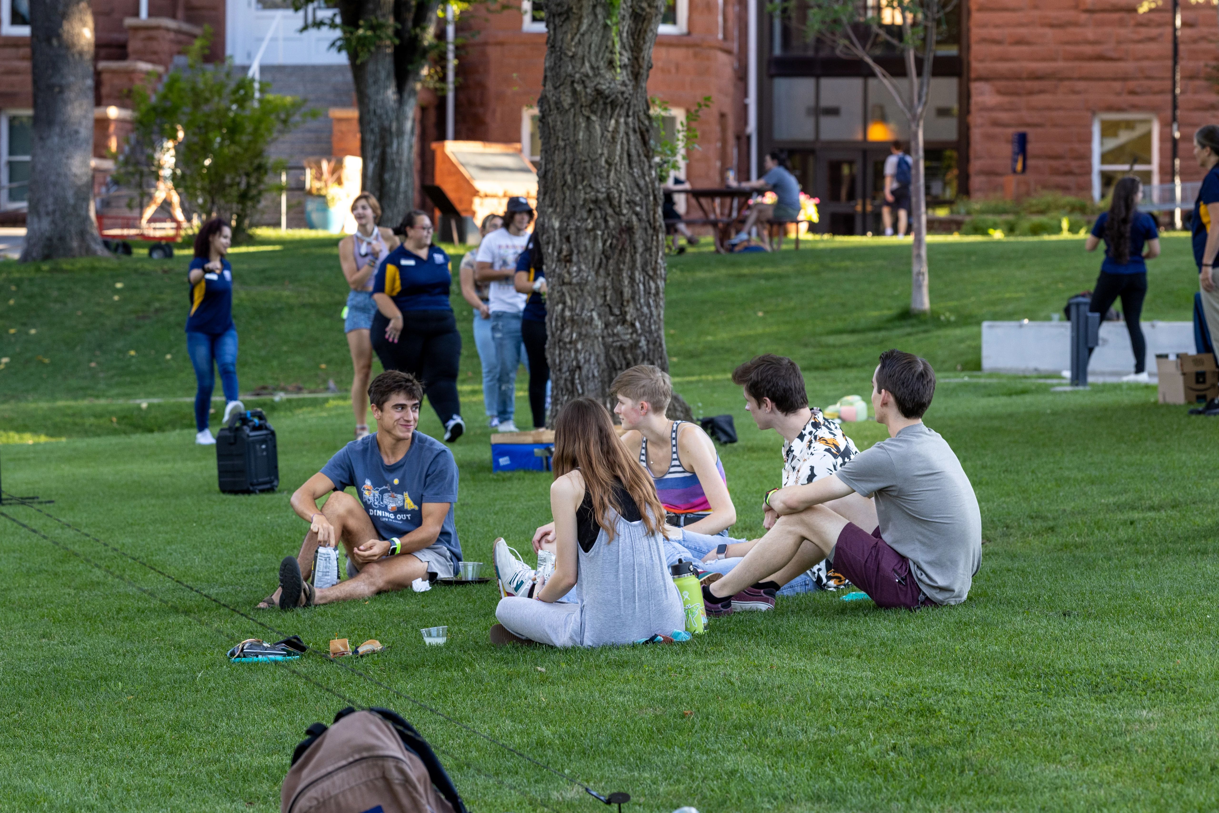Group of students eating together on grass field at N A U welcome picnic.