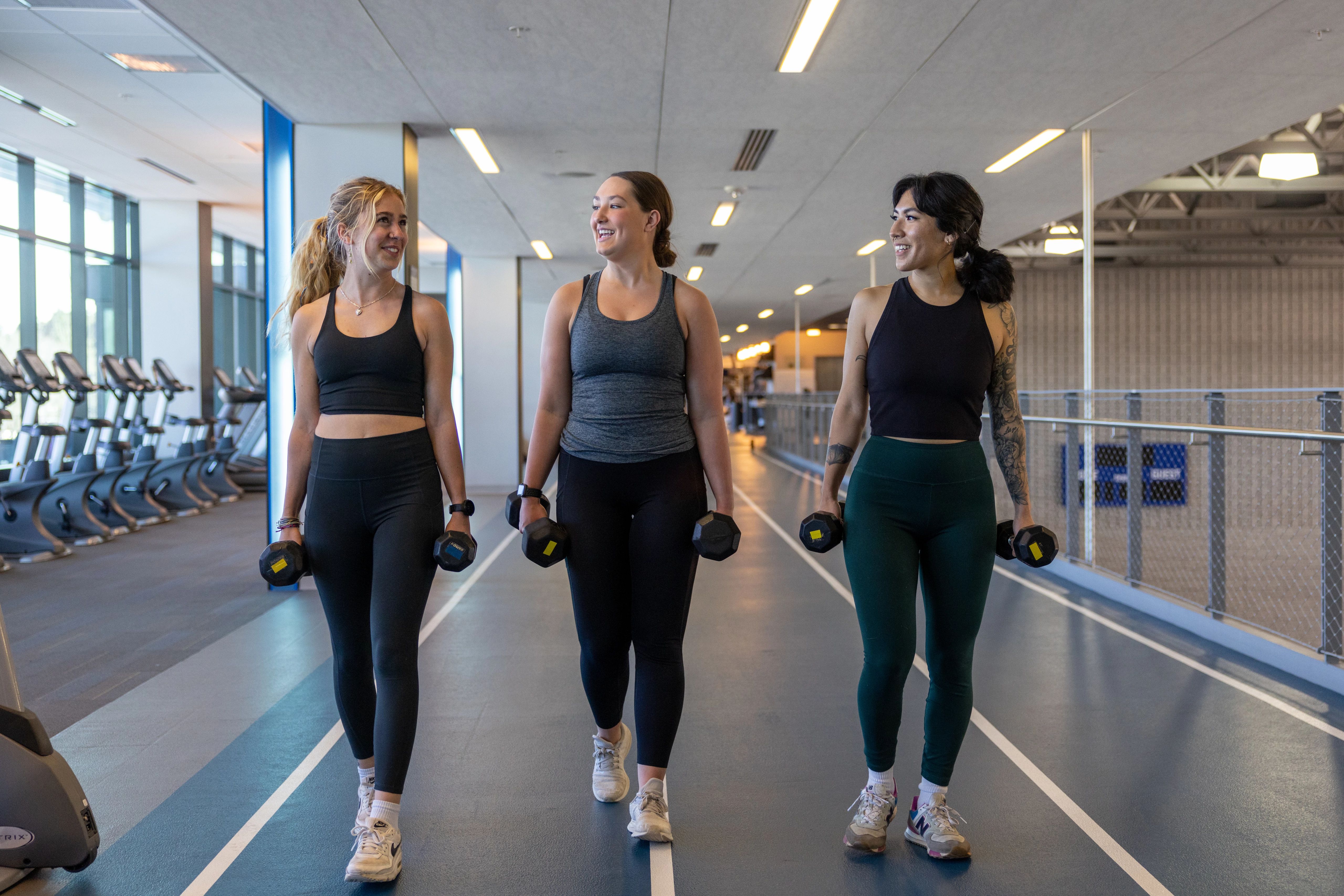 Three students holding weights while waking at the gym.