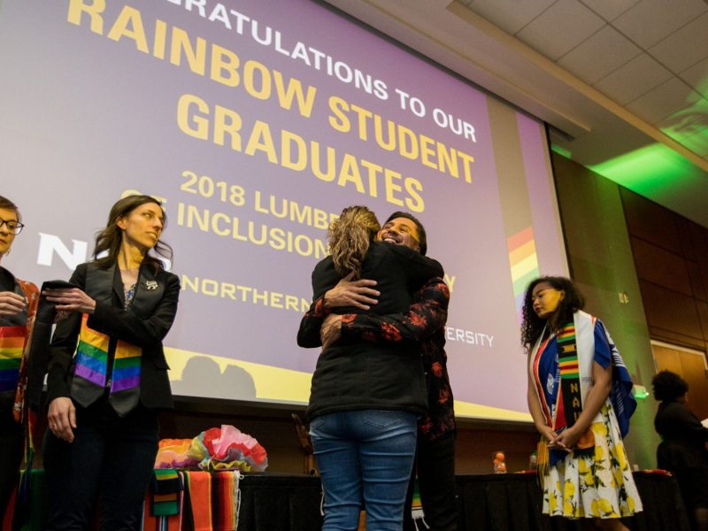 Students hug in front of a presentation screen that reads "Rainbow Student Graduates"